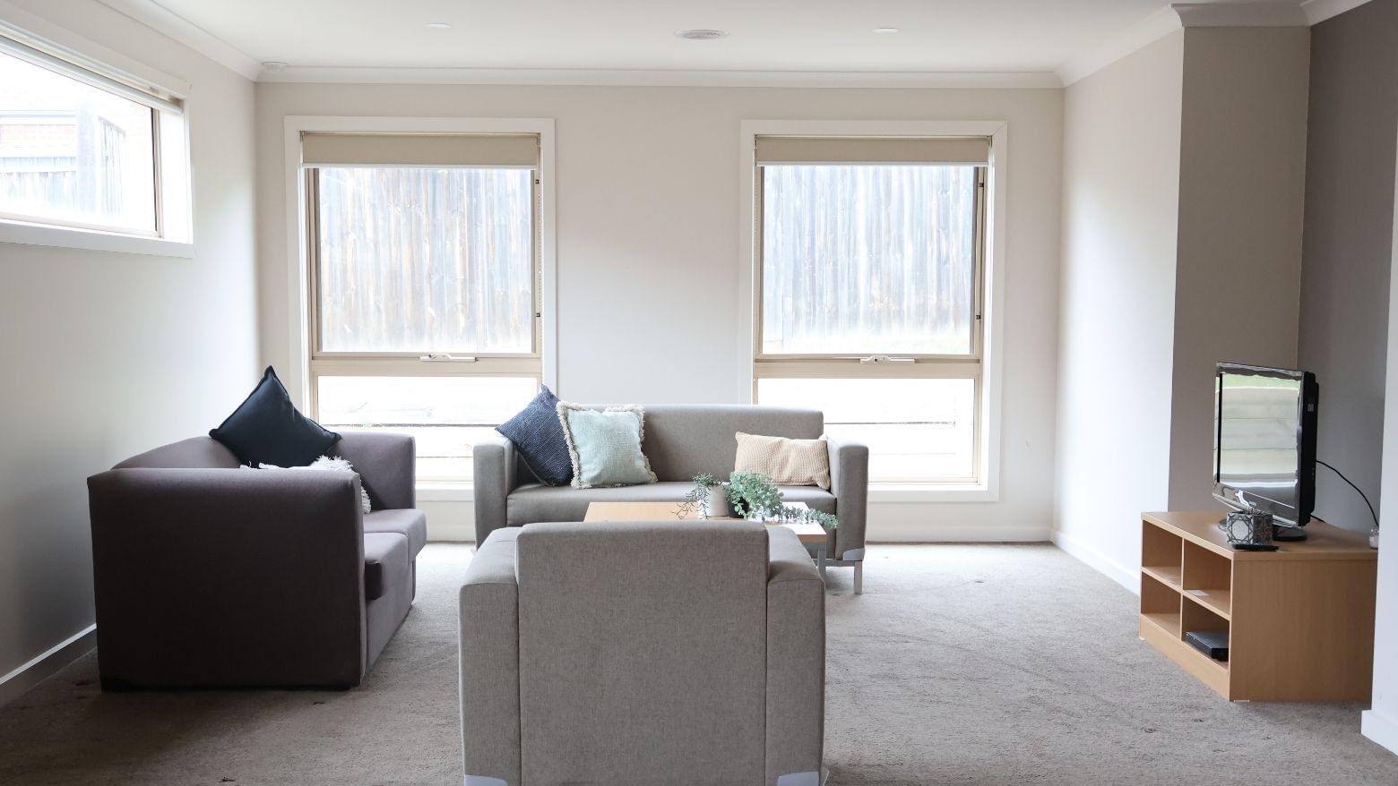 Living room with two couches, TV, and windows at La Trobe University Regional Housing – Melton.