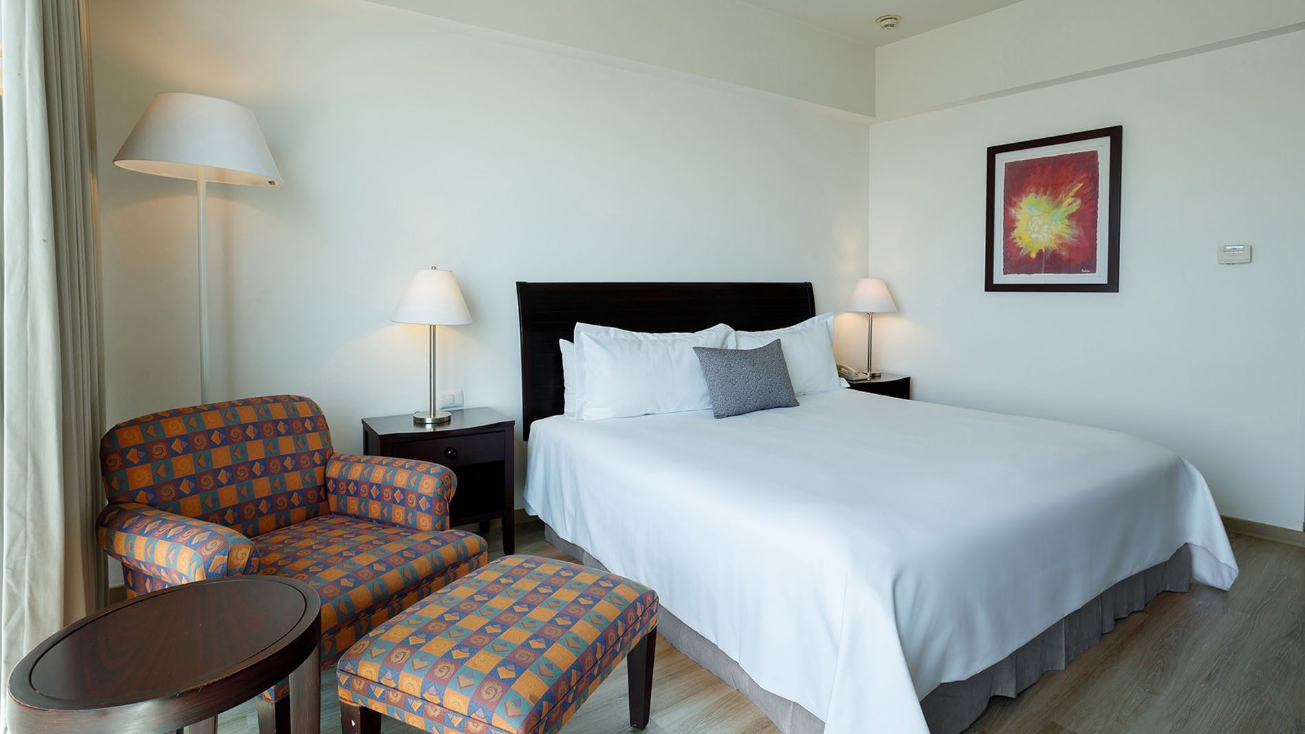 King Camino Real Club featuring a patterned armchair with ottoman, white bed, and colorful artwork at Camino Real Pachuca