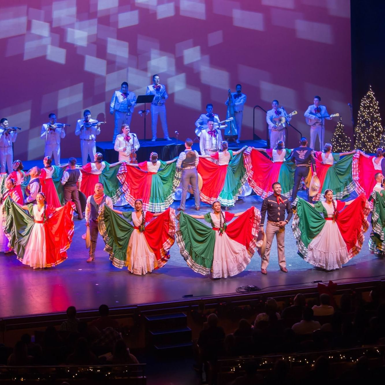 Photo of Nochebuena event showing performers on stage in large Mexico flag colored dresses in front of a live band