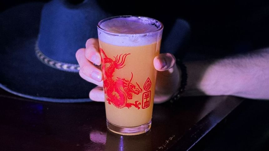 Pint glass featuring a red dragon print held by a person on a dark table at Media Sangre craft brewery in Araiza Calafia