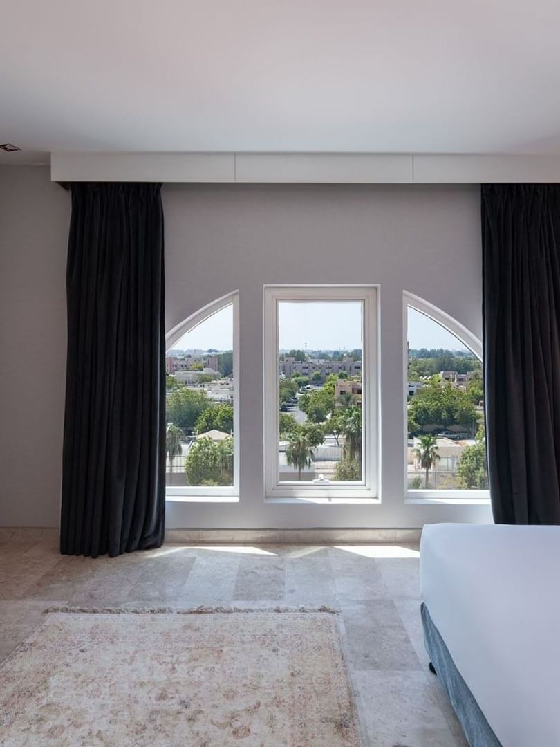 White bed by arched windows and a wooden desk with a wall-mounted television in Deluxe Room City View
