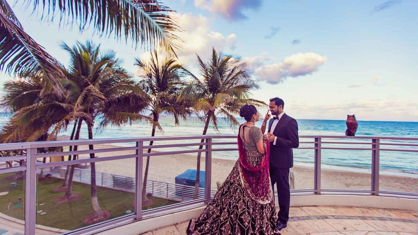 Couple in formal attire on a beachfront balcony at sunset at Diplomat Beach Resort