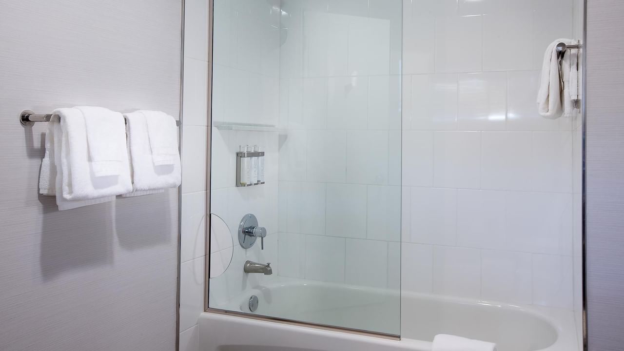 A clean bathroom with a glass shower enclosure, white towels, and a white bathtub.
