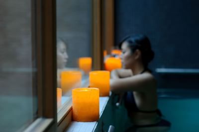 Velas naranjas brillantes junto al borde de la piscina bajo luz tenue en el sereno Noi Spa de NOI Vitacura