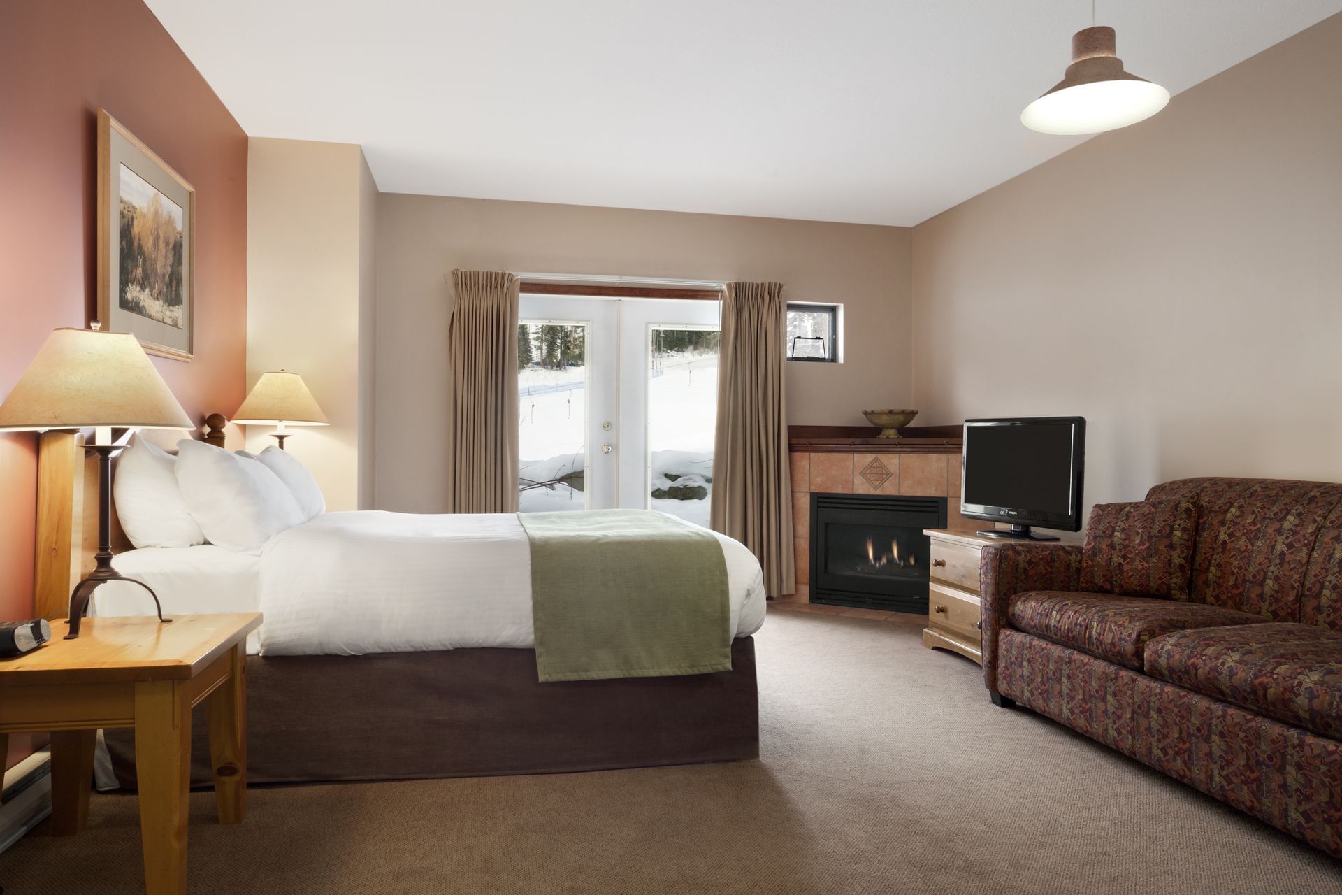 Bed and sofa in hotel room with fireplace and view of ski slopes
