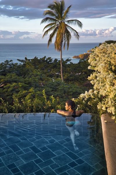 woman swimming in infinity pool overlooking tropical beach