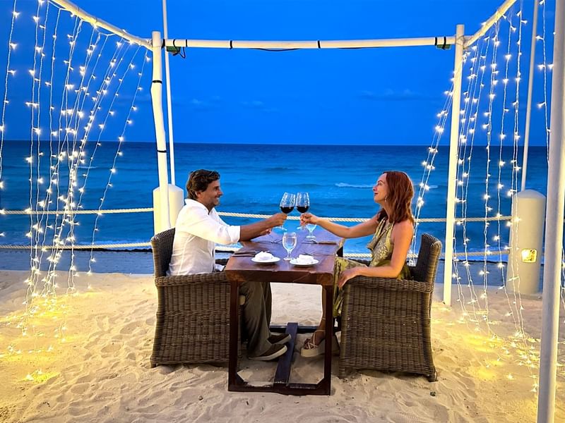 Couple celebrating with wine glasses at a table with beach view at Fiesta Americana