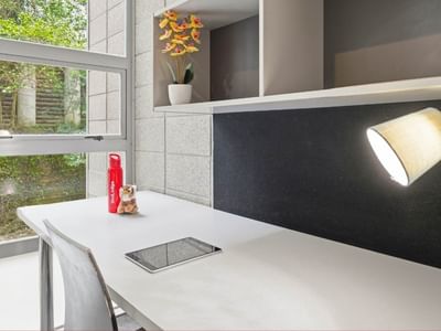 Cozy workspace with desk, chair, tablet, and lamp at Student Living Auckland Beach.