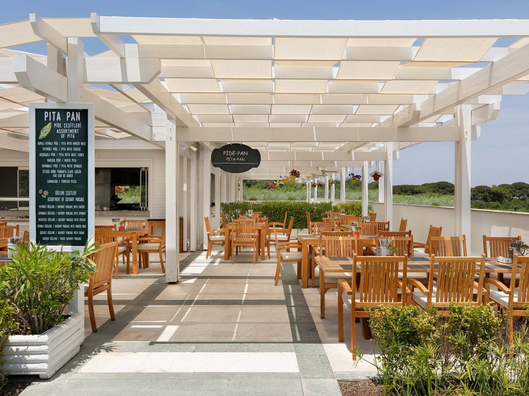 Dining tables and chairs arranged with outdoor view in Pita Pan Restaurant at Titanic Deluxe Golf Belek
