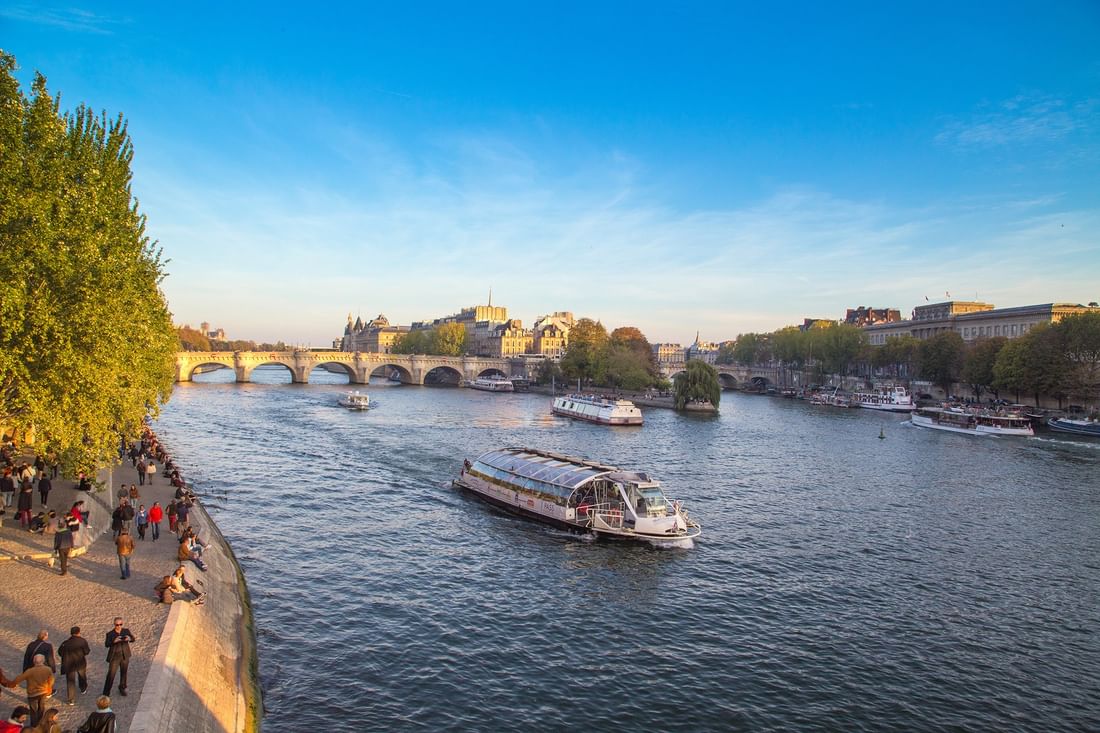 River boat cruising by an arched stone bridge under a clear sky in the city of Paris near Hotel Westminster Paris