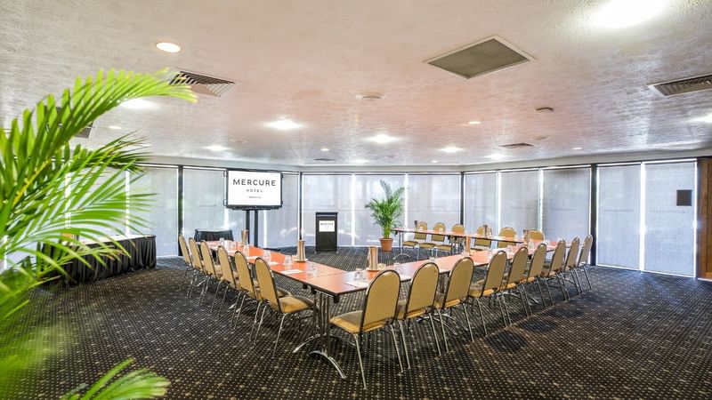 Eacham Room with large U-shaped table, chairs, and a TV screen at Mercure Hotel Townsville
