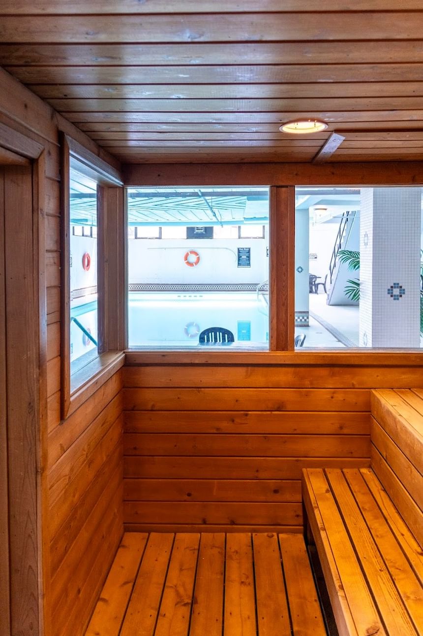 Inside a wooden sauna with tiered benches, looking out a large window toward an indoor pool at Rodd Grand Yarmouth