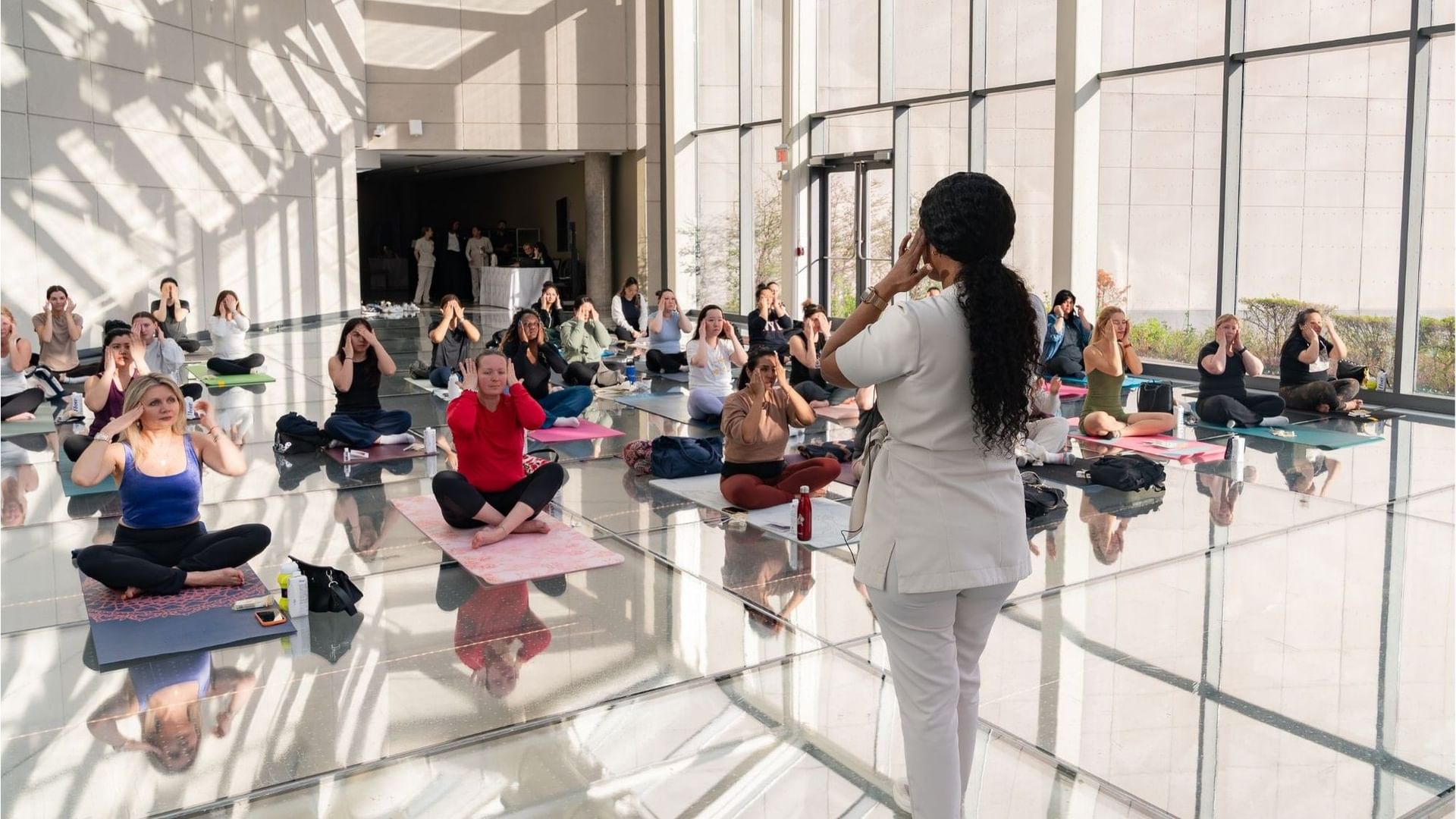 Wellness specialist guiding seated guests through facial exercises in a bright glass-walled studio at Hotel X Toronto