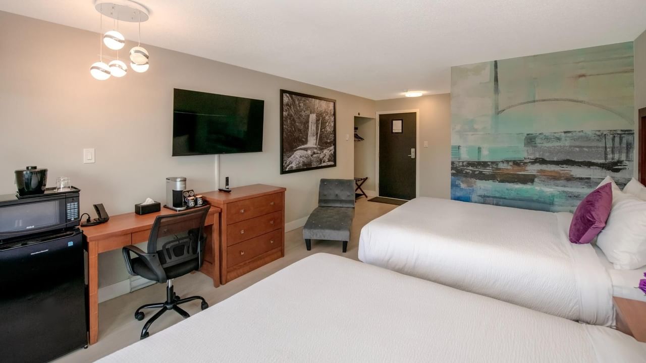Two beds, a desk with chair, a coffee maker and a microwave in a hotel room.