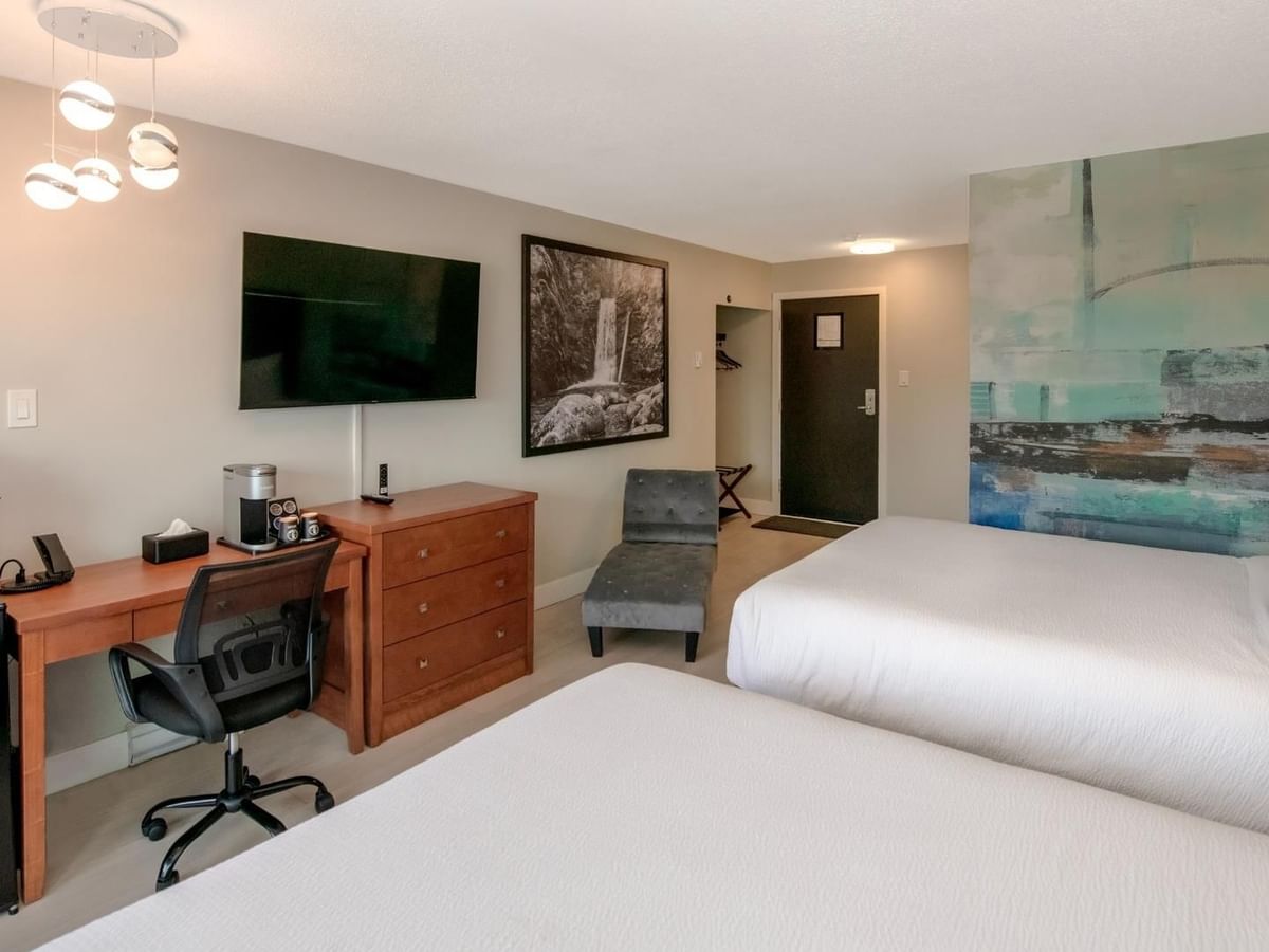 Hotel room with two beds, a desk, a TV, a mini-fridge and a modern art wall.