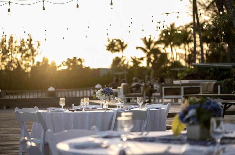 Set dining table with white chairs under hanging string lights at sunset at Warwick Paradise Island Bahamas