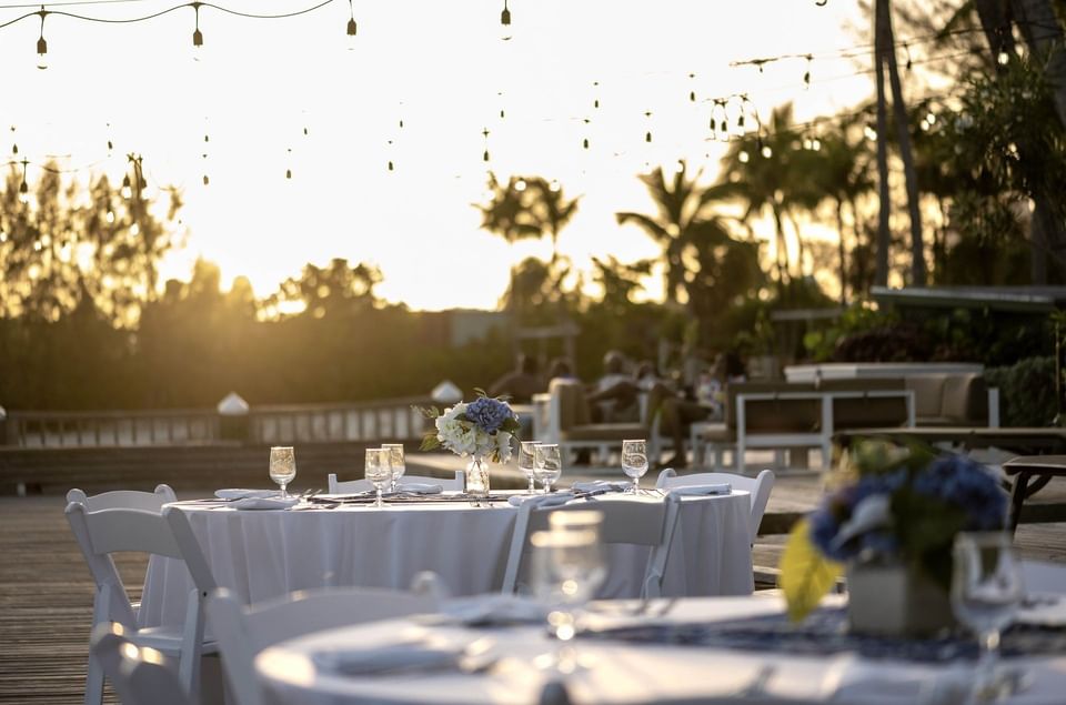 Set dining table with white chairs under hanging string lights at sunset at Warwick Paradise Island Bahamas