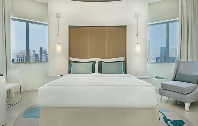 Luxury king bedroom featuring hanging side lamps and a grey armchair near windows at DAMAC Maison Mall Street