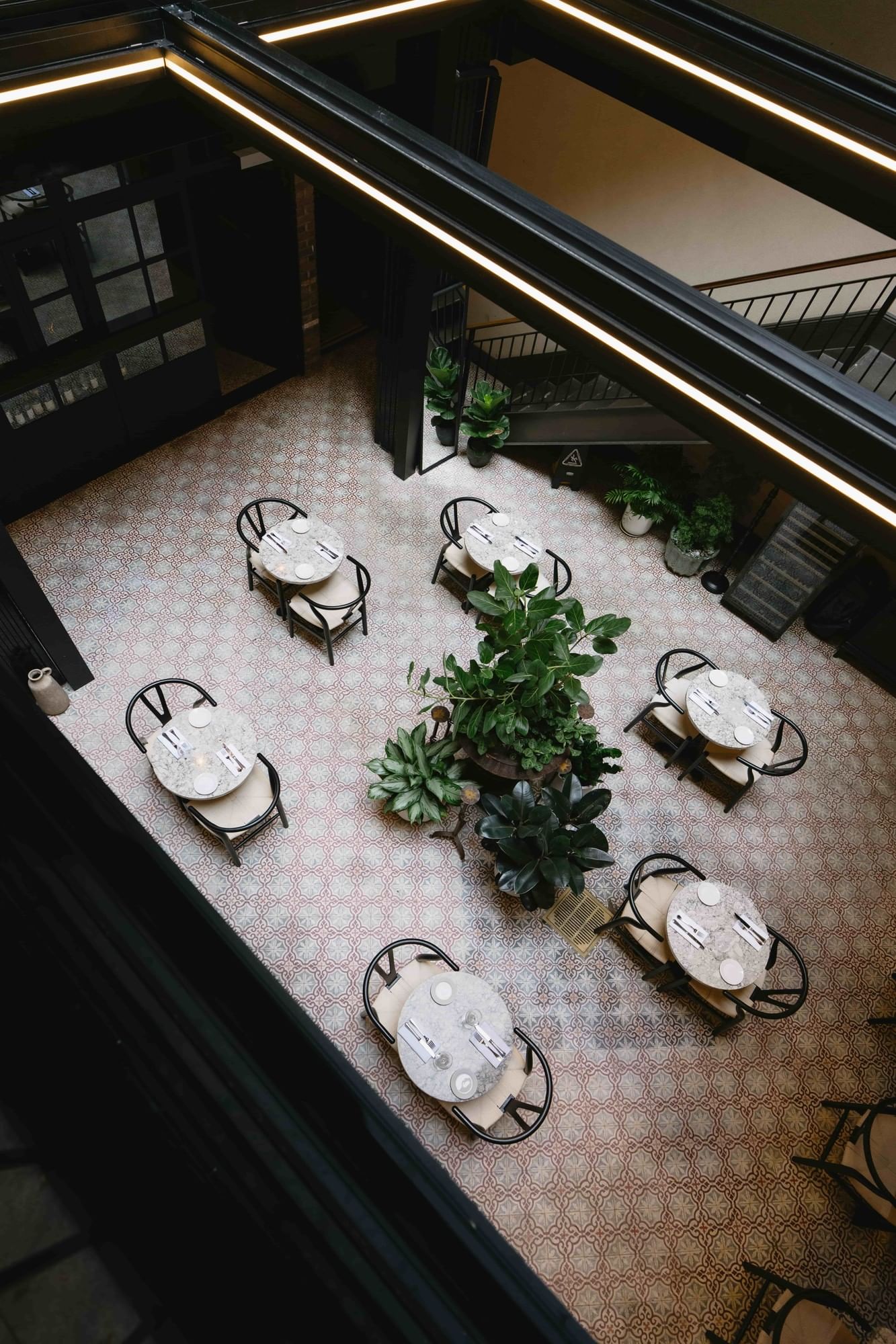 A dining area with several round tables and chairs, and plants in the center.
