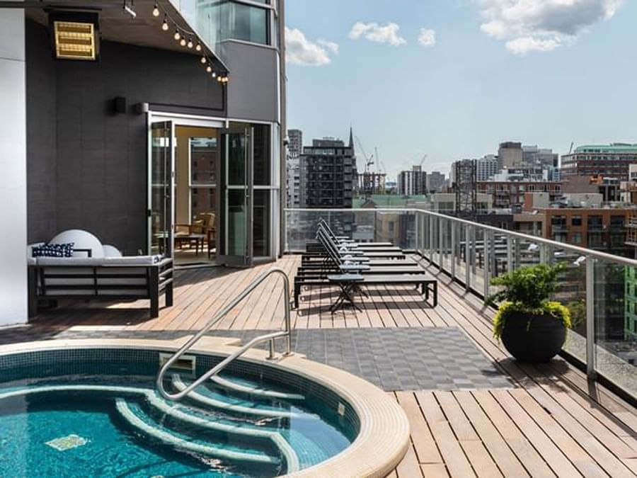 Rooftop wooden deck with a circular hot tub and lounge chairs at Warwick Le Crystal Montreal