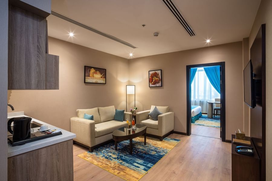TV lounge with a cozy sofa near an open door leading to the bedroom in Junior Suite at Naviti by Warwick Dammam