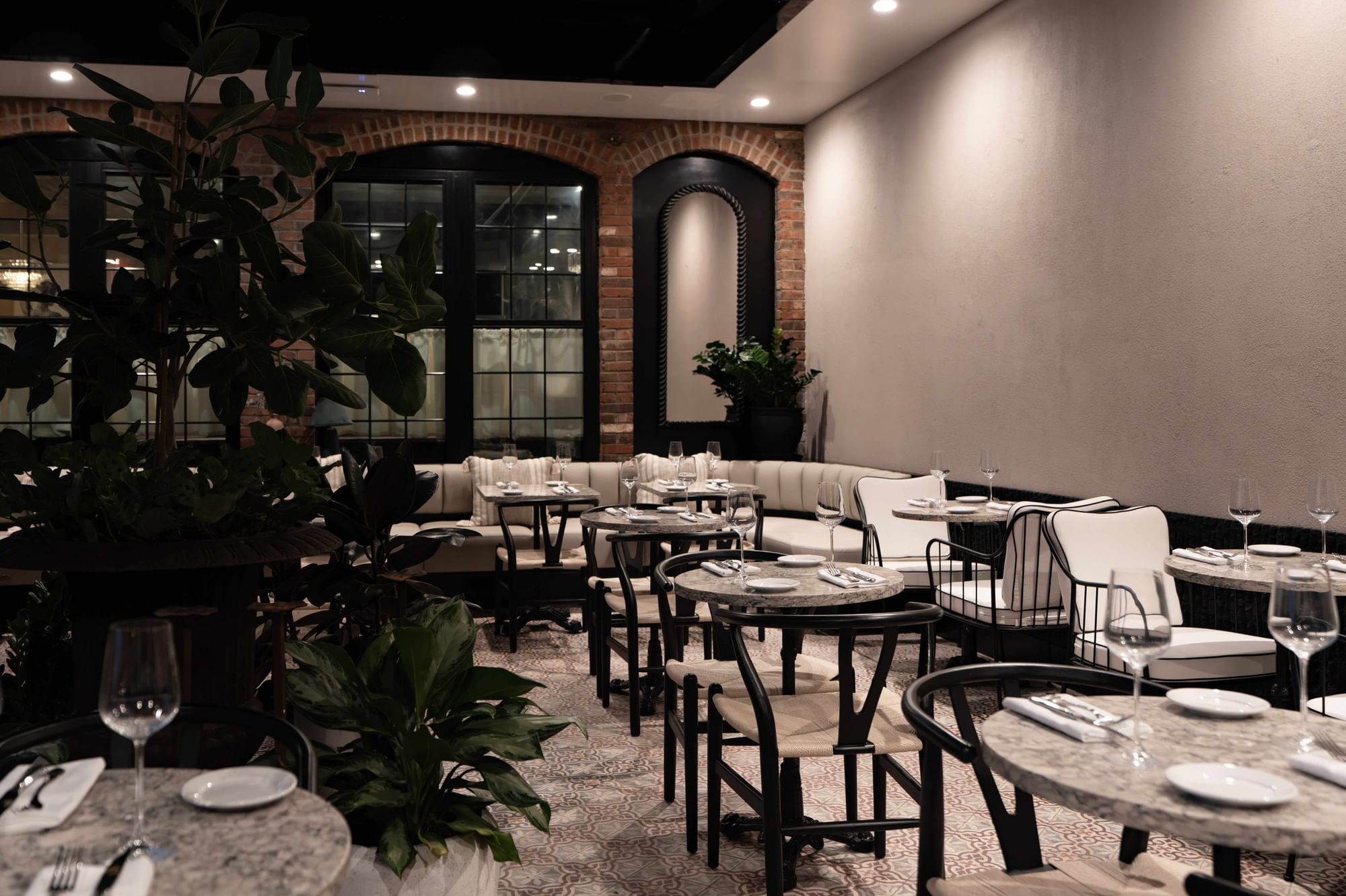 A dining area with round tables and chairs, a sofa, and large windows.