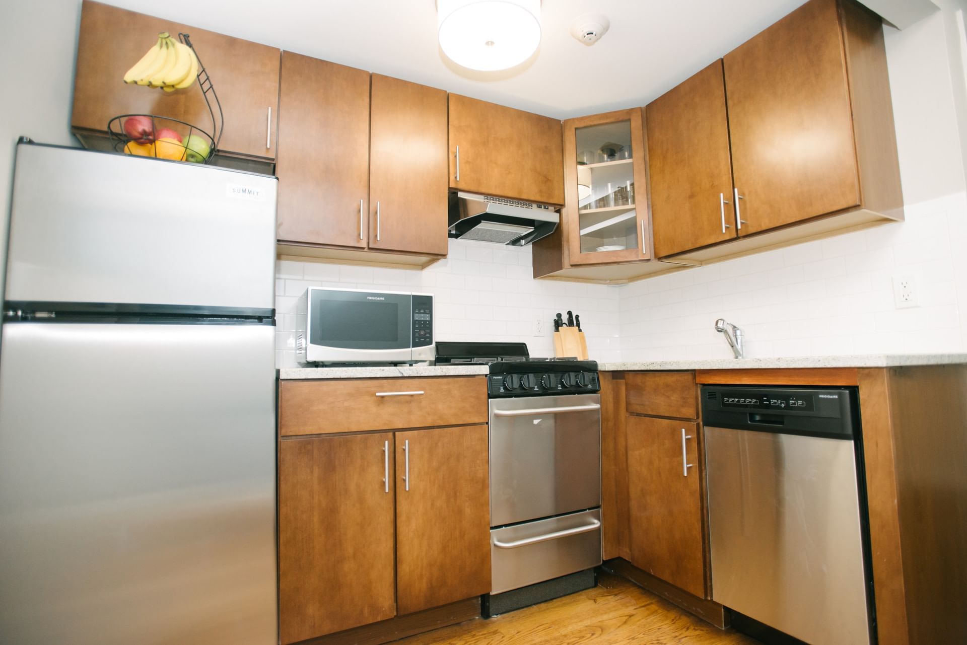 A kitchen with stainless steel appliances, wood cabinets, and a fruit basket on top of the refrigerator.