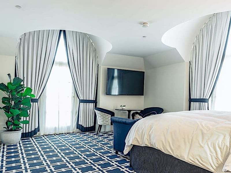 Spacious guest room at El Prado Hotel, with a large bed, navy carpet, and curved curtains