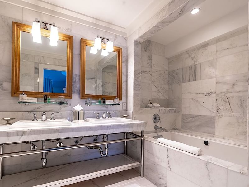 Elegant marble bathroom at El Prado Hotel, with double vanity, gold mirrors, and a deep soaking tub