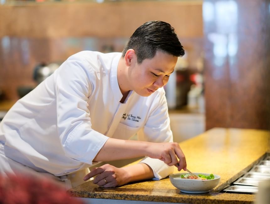 Chef in a white uniform carefully adding garnishes to a bowl of fresh salad on a countertop at Park Hyatt Saigon