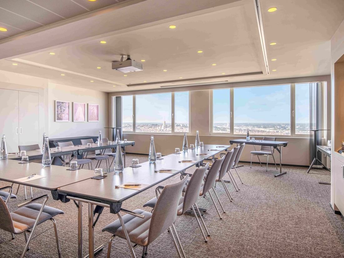 Meet 25 One Meeting room with table, chairs, and city view through large windows at The Hotel Brussels