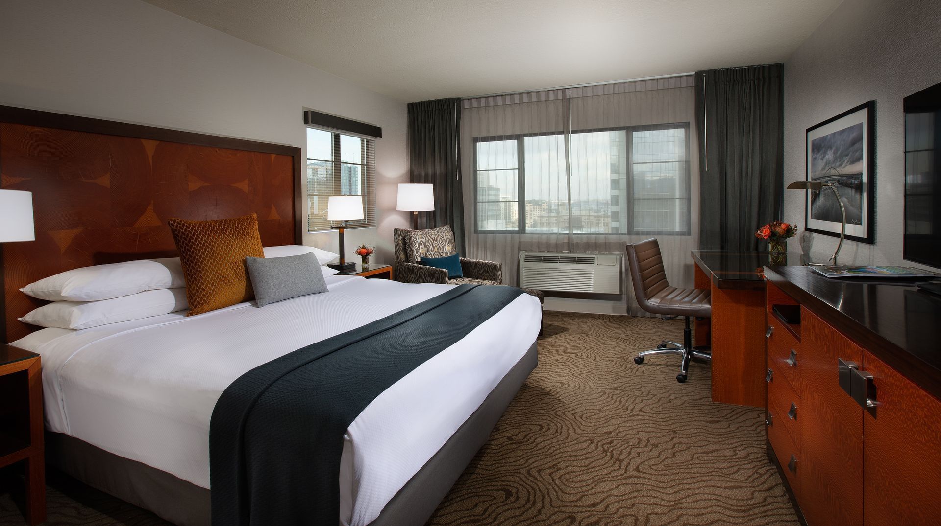 A hotel room with a large bed, desk, chair, and window.