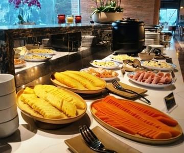 Breakfast buffet counter with sliced pineapple and papaya platters near cured meats and orchids at Hotel B3 Sibelius
