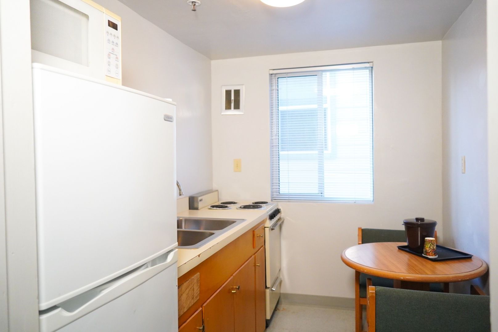 A compact kitchenette with a refrigerator, stove, sink, and small dining area.