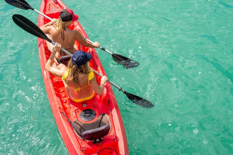 Two women paddling a red kayak  in the ocean near The Diplomat Resort
