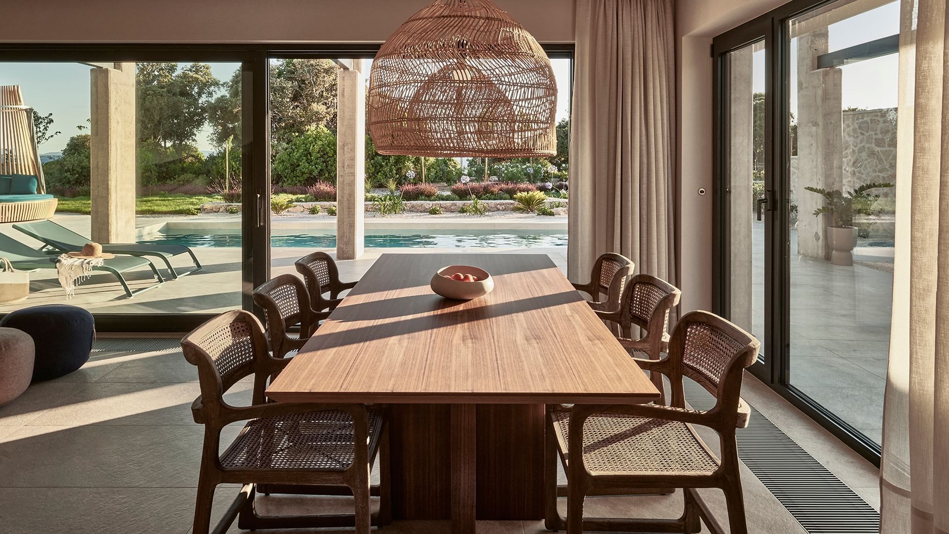 Dining room with wooden table, and wicker chairs, overlooking a pool in Villa Anastasia at Falkensteiner Resort Punta Skala