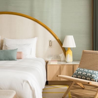Bedroom with arched headboard, white bedding, wooden nightstand, lamp, and wicker chair.