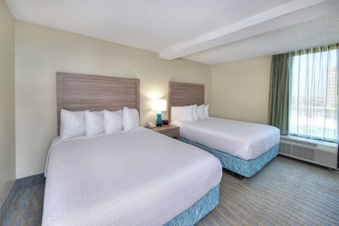 A hotel room with two beds, a window, and a carpeted floor.