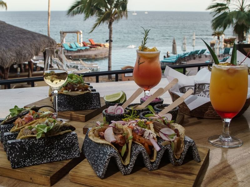Tacos and two cocktails served on a wooden table with ocean views at Sirenas, Hacienda Del Mar Los Cabos