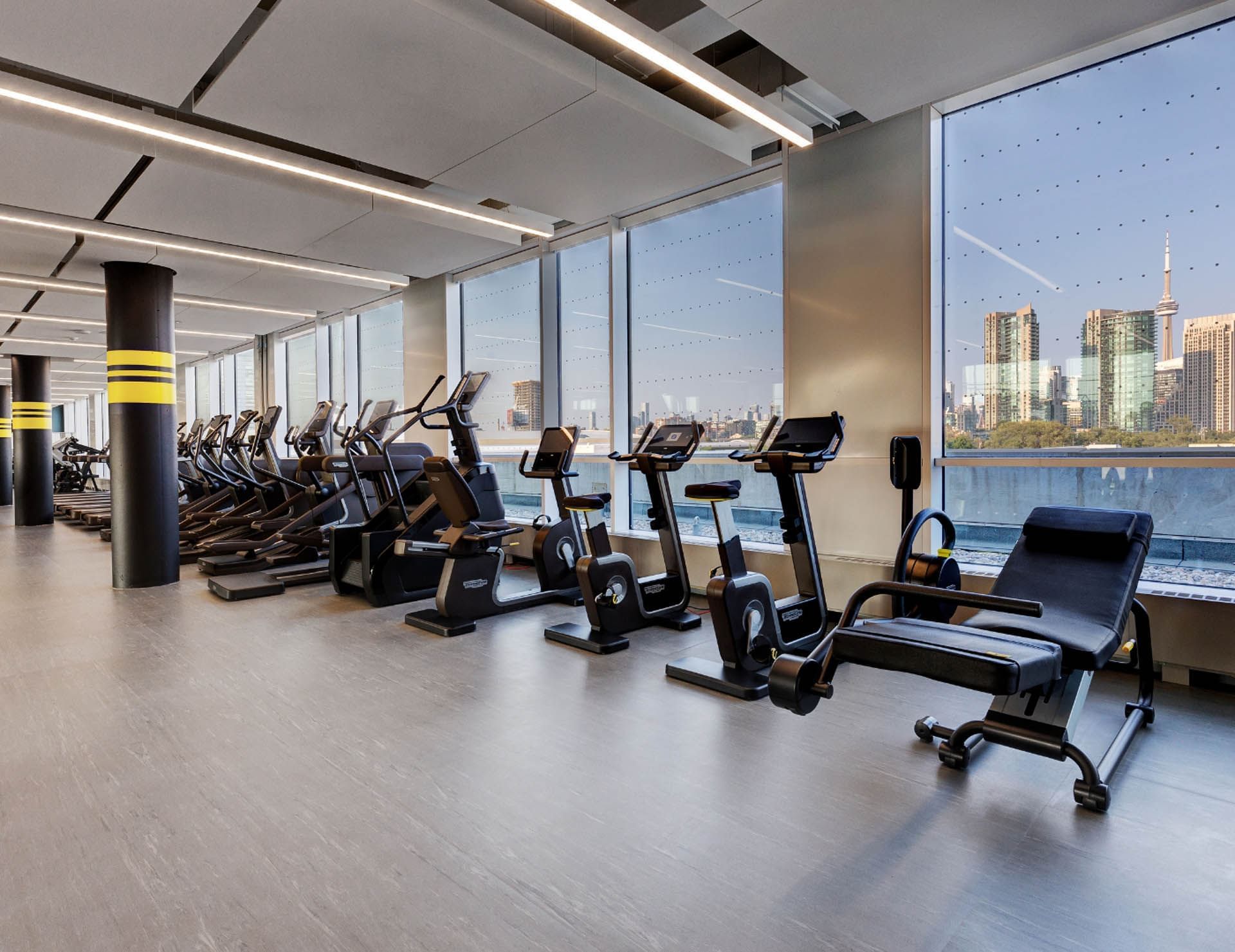 Modern gym with rows of cardio equipment facing floor-to-ceiling windows with Toronto skyline views at Hotel X Toronto