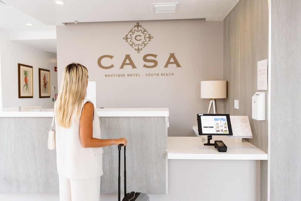A woman stands at the reception desk of a hotel lobby.