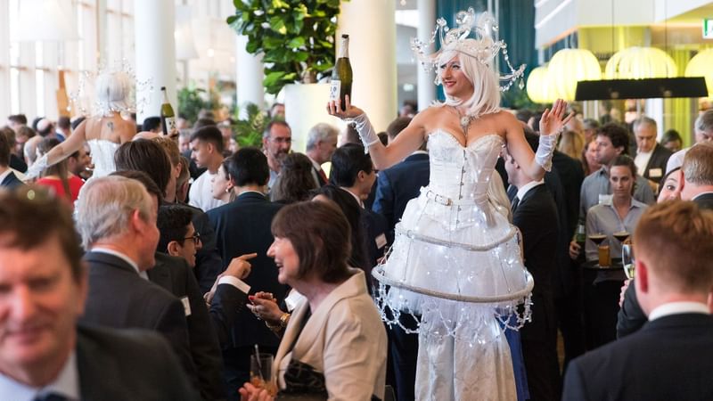 Performer in a white gown adorned with lights and holding bottles in events by Ternary at Novotel Sydney on Darling Harbour