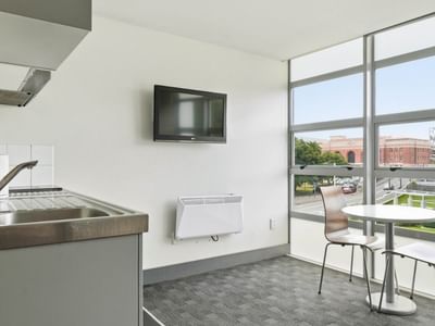 Modern kitchen with sink, TV, and dining table by large window at Student Living Auckland - Beach.