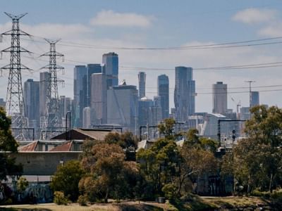 Melbourne CBD skyline with tall buildings and power towers behind trees and structures.