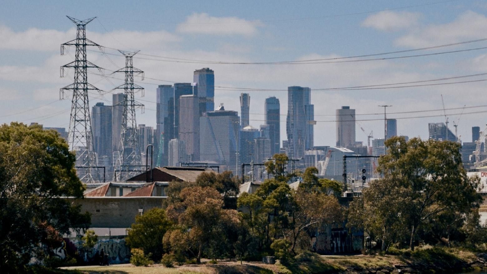 Melbourne CBD skyline with tall buildings and power towers behind trees and structures.
