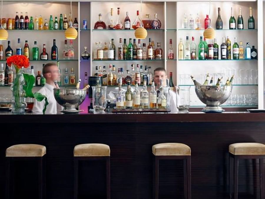 The Lounge Bar with a wooden counter and mirrored shelves lined with various liquor bottles at Warwick Reine Astrid - Lyon