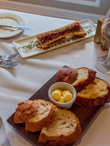 Sliced artisan bread with a bowl of butter under a meat appetizer in The Landmark Prime Rib at Warwick Melrose Dallas