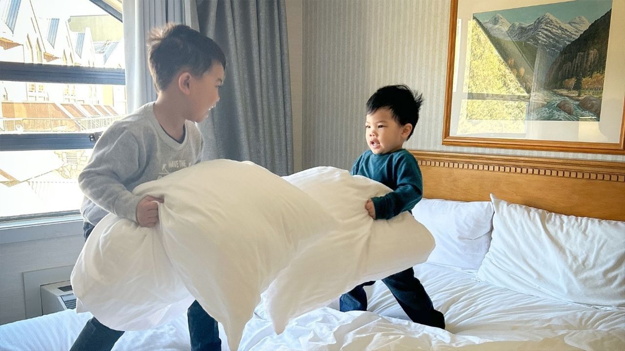 Two children playfully making a bed together in a hotel room