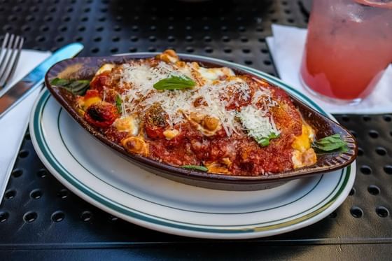 Baked pasta dish topped with melted cheese and garnished with fresh basil at Windsong Resort On The Reef