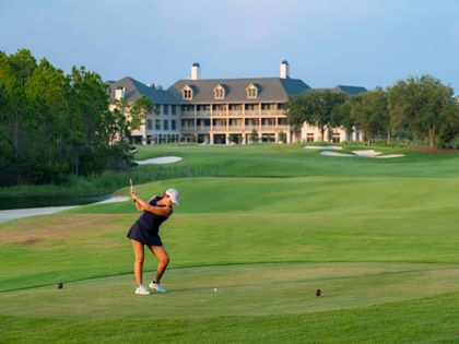 Golfer teeing off on manicured fairway with clubhouse and sand traps in background at Camp Creek Inn, Inlet Beach.